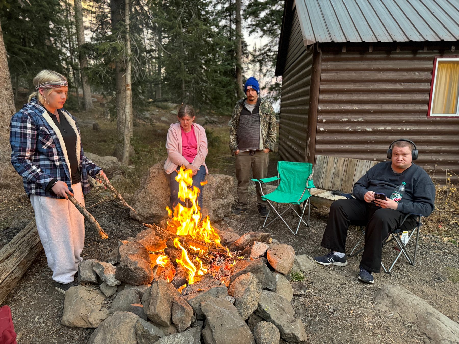Residents around a fire beside a mountain cabin